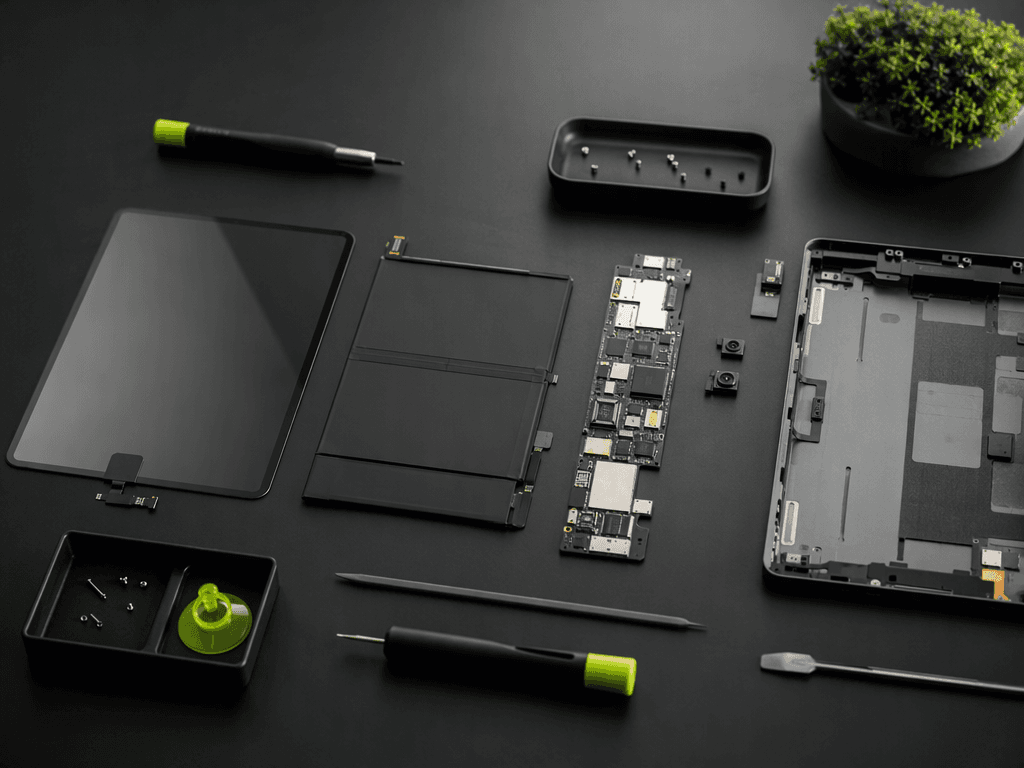 A tablet disassembled into glass, battery, board, and frame on a dark desk